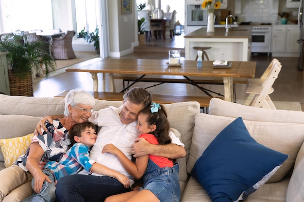 Foto vorderansicht kaukasischer großeltern, die auf einem sofa sitzen und ihren kleinen enkel und ihre enkelin umarmen und lächeln. familie genießt die zeit zu hause, lifestyle-konzept