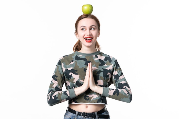 Vorderansicht lächelnde junge Frau mit grünem Apfel auf dem Kopf auf weißem Hintergrund