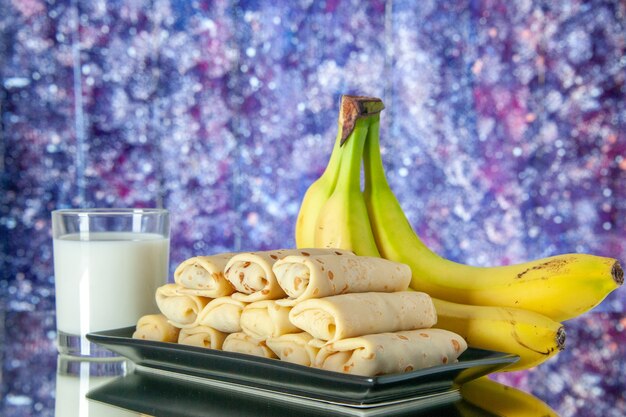 Vorderansicht lecker gerollte Pfannkuchen mit Bananen und Milch auf violettem Hintergrund Morgen süße Kuchenfarbe Zuckermilch Dessertfrucht