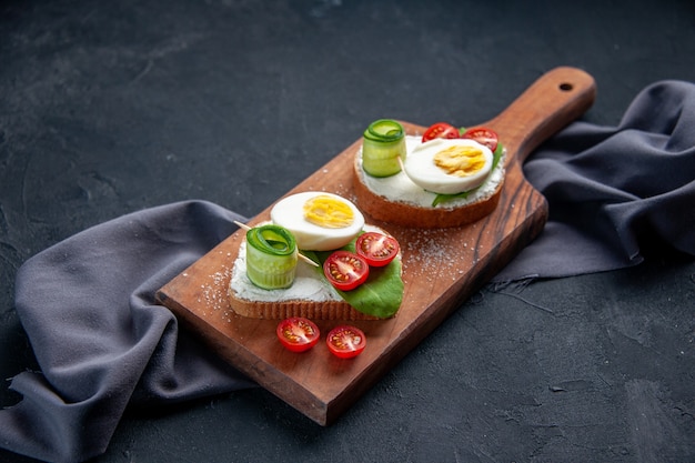 Vorderansicht leckere Sandwiches mit Tomaten, Gurken und Eiern auf dem Schneidebrett dunkler Hintergrund Mahlzeit Burger Essen Mittagessen Sandwich Toast Snack