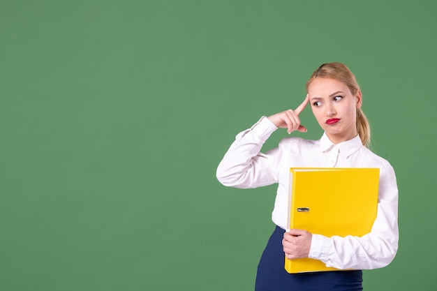 Vorderansicht Lehrerin, die gelbe Dateien auf grünem Hintergrund hält Buch Studie Uniform Lektion Bibliothek Schüler Schule Arbeit Frau