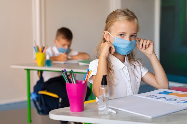 Foto vorderansicht-mädchen, das ihre medizinische maske in der klasse aufsetzt