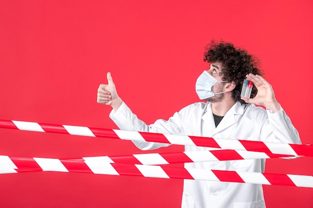 Foto vorderansicht männlicher arzt in medizinischer uniform, der flaschen auf rotem hintergrund hält, quarantäne-kovid-healing-gesundheitsgefahr-warnung isolation