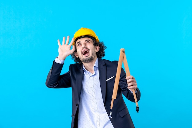 Vorderansicht männlicher Baumeister in Helm mit Holzgerät auf blauem Hintergrund arbeiten Baujob Business Architektur Design Konstrukteur