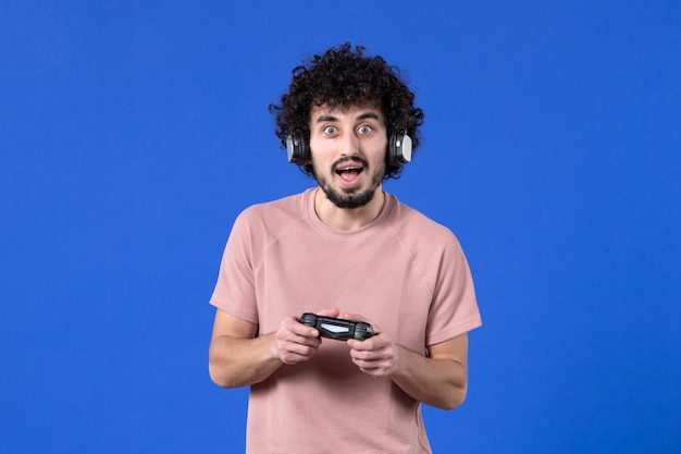 Vorderansicht männlicher Spieler mit Gamepad und Kopfhörern, die Videospiel auf blauem Hintergrund spielen virtuelles Video Fußball Teen Erwachsener gewinnender junger Freude Spieler