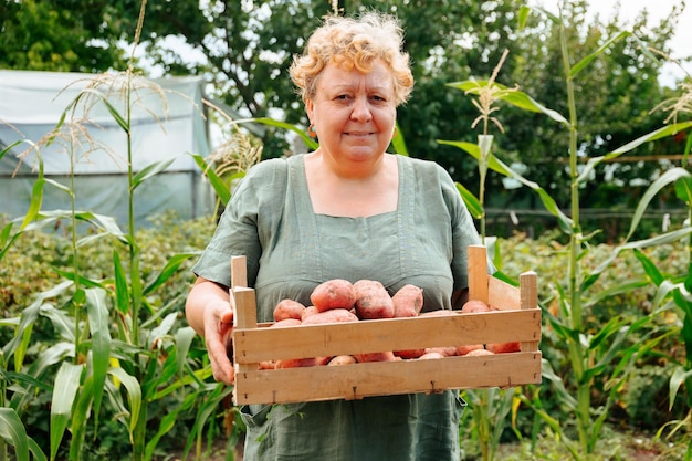 Vorderansicht mit Blick auf die Kamera Ältere Frau steht im Garten mit Kartoffelernte in den Händen