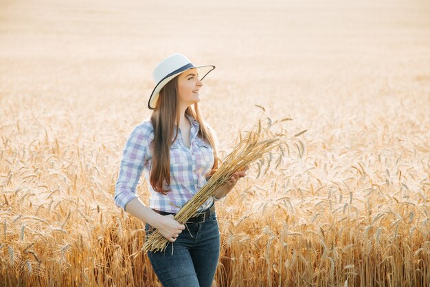 Vorderansicht Porträt einer jungen Bäuerin mit Hut über einem goldenen Weizenfeld, das einen Haufen Weizen hält...