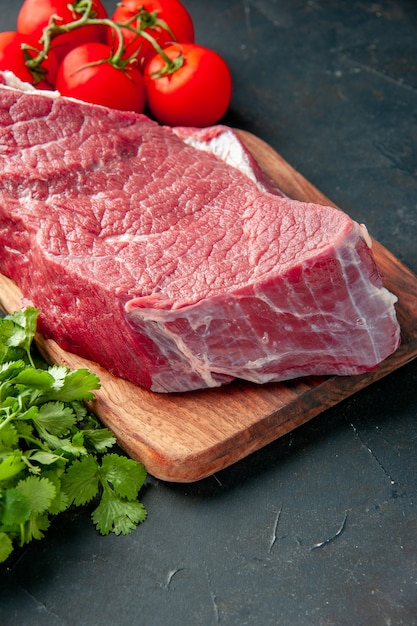 Vorderansicht rohe Fleischscheibe mit roten Tomaten und Grüns auf dunkelgrauem Hintergrundfarbe Metzger Essen Fleisch Essen Grill kochen