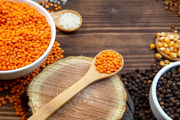 Vorderansicht rohe Grütze Linsen Reiskörner und Buchweizen mit Pfeffer auf braunem Hintergrund Farbe Abendessen Pflanzenfutter Mahlzeit frische Samen Küche