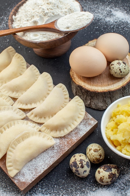 Vorderansicht rohe kleine heiße Kuchen mit Mehl, Kartoffelpüree und Eiern auf dunklem Hintergrund Kuchenteigkuchen backen Speiseöl Keksofen