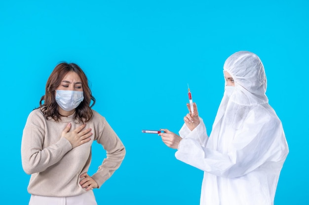 Vorderansicht Ärztin im Schutzanzug mit kranken Patienten auf blauem Hintergrund medizinisches Virus covid pandemische Krankheit Wissenschaft Gesundheit