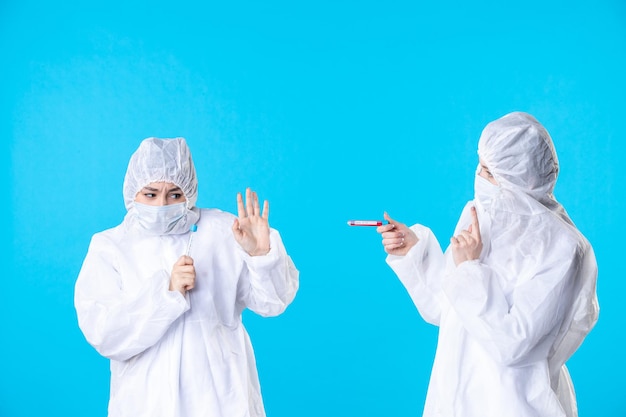 Vorderansicht Ärztinnen in Schutzanzügen und Masken, die Flaschen auf blauem Hintergrund halten Virus Health Science Covid Hospital Medical Pandemie