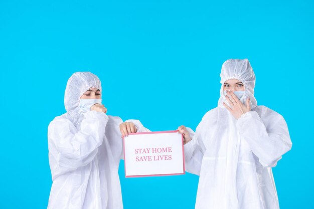 Vorderansicht Ärztinnen in Schutzanzügen und Masken mit Warnhinweis auf blauem Hintergrund Gesundheitswissenschaft covid-pandemische medizinische Isolation