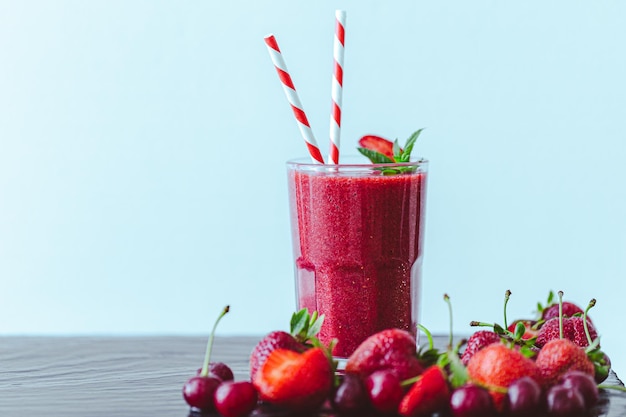 Vorderansicht von Beerensaft oder Smoothie mit frischen Erdbeeren und Kirschen auf blauem Hintergrund