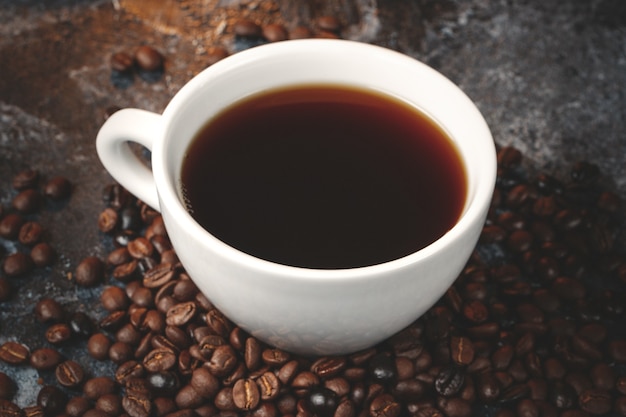 Vorderansicht von braunen Kaffeesamen mit Tasse Kaffee auf dunkler Oberfläche