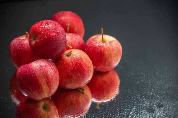 Vorderansicht von gestapelten frischen feuchten roten Äpfeln auf dunklem Wellenhintergrund