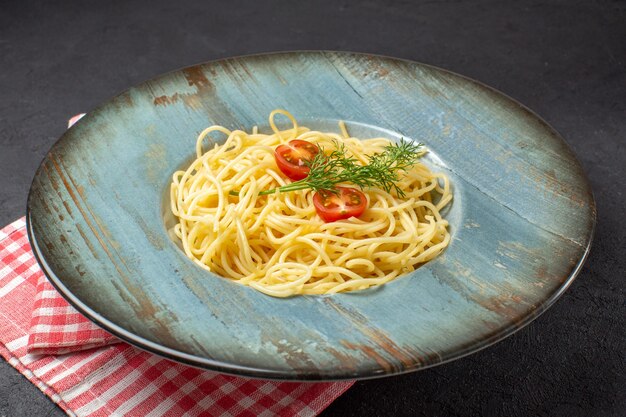 Vorderansicht von köstlichen Spagetti, serviert mit Tomatengrün auf rot gestreiftem Handtuch auf schwarzem Hintergrund