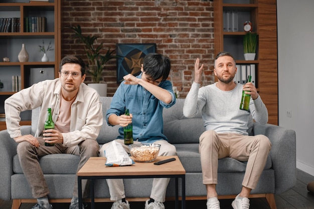 Vorderansicht von Männern, die sich ein Fußballspiel im Fernsehen ansehen und ein Bier trinken