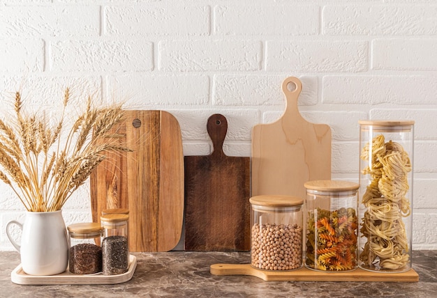 Vorderansicht von umweltfreundlichen Küchenutensilien aus Holz und Glas auf einer modernen Küchenarbeitsplatte und einer weißen Backsteinwand. Stilvoller Küchenhintergrund