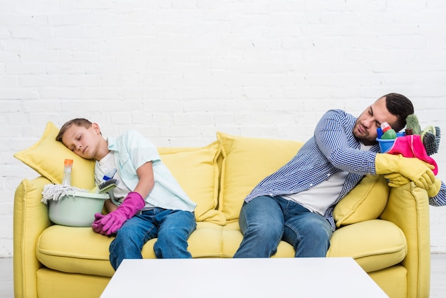 Vorderansicht von Vater und Sohn, die nach Reinigung auf Sofa ruhen