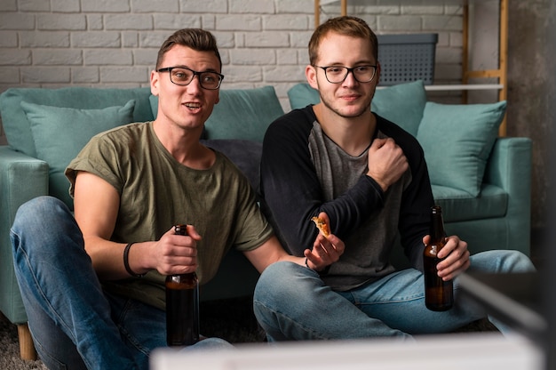 Vorderansicht von zwei männlichen Freunden, die Bier trinken und Sport im Fernsehen schauen