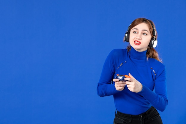 Vorderansicht weiblicher Spieler mit Gamepad, der Videospiel auf blauem Hintergrund spielt Spieler gewinnt erwachsene virtuelle Freude Gewinner Jugend online fröhliches Video