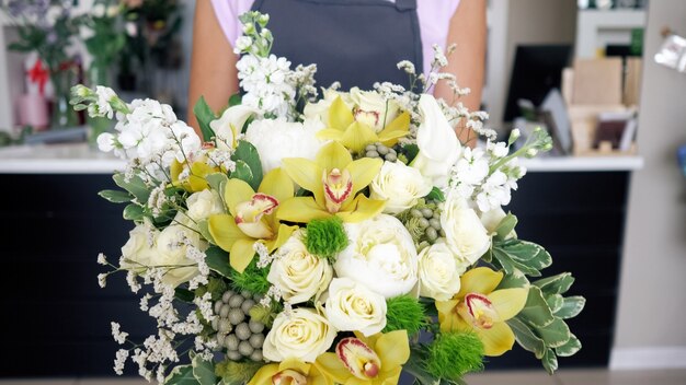 Vorführung von Blumenarrangements im Floristikstudio. Floristenfrau kommt mit schönem Rosen- und Lilienstrauß im Blumenladen. Frau hält riesigen Haufen in ihren Händen, Detailansicht.