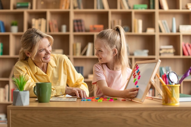 Vorschulerziehung Fröhliche professionelle Lehrerin, die mit einem süßen Mädchen trainiert, das Buchstaben liest und Wörter macht