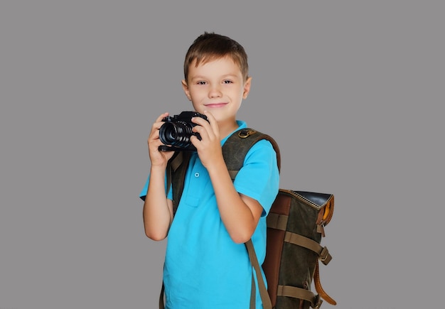 Vorschuljunge, der Fotos mit einer professionellen Fotokamera macht. Isoliert auf grauem Hintergrund.