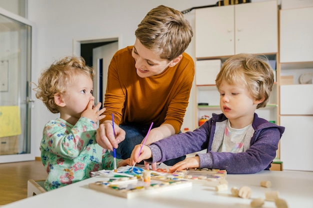 Vorschullehrerin malt mit zwei Kindern im Kindergarten