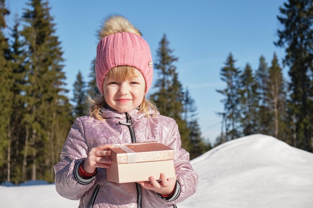 Vorschulmädchen mit glänzender Geschenkbox außerhalb des Wintertages bei sonnigem und kaltem Wetter
