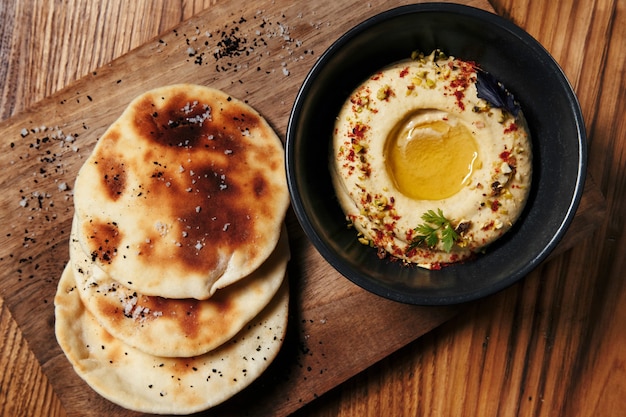 Vorspeise Hummus aus dem Nahen Osten, serviert mit frischem Fladenbrot und Kräutern auf Holzhintergrund-Draufsicht