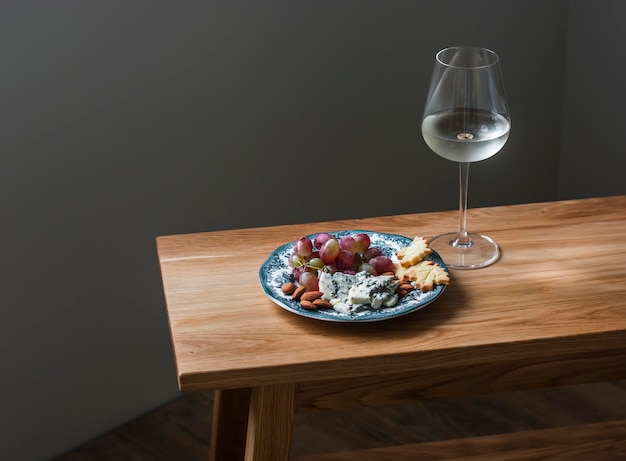 Vorspeisenteller mit Trauben-Gorgonzola-Nuss-Cracker und einem Glas Weißwein auf einem Holztisch