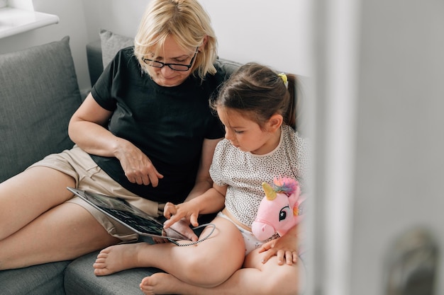 Vovó e menina pré-escolar usando tablet juntos em casa no sofá tempo de união familiar