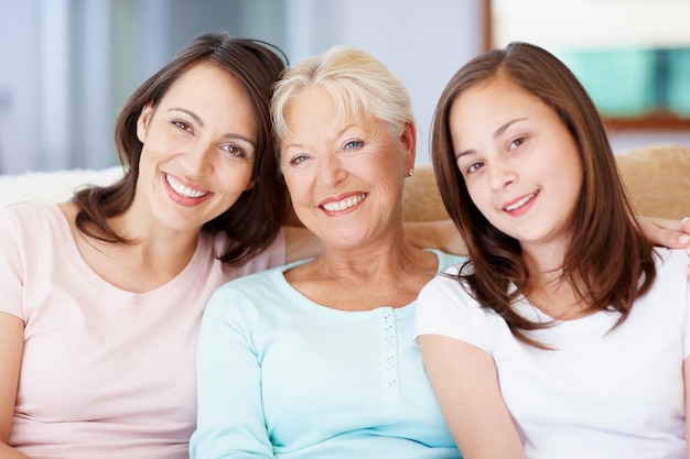 Vovó mãe e eu Três gerações de meninas sentadas juntas no sofá da sala juntas e sorrindo