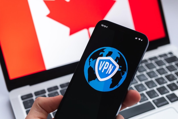 VPN en Canadá Concepto de Internet seguro y seguro Privacidad Mano con teléfono móvil y aplicación VPN Bandera y computadora portátil en la foto de fondo