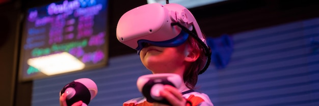 Vr-Spiel und Virtual-Reality-Kid-Boy-Gamer sechs Jahre alt Spaß beim Spielen auf futuristischem Simulationsvideospiel in 3D-Brille und Joysticks im Unterhaltungs-VR-Raum mit Technologie und Neonlicht-Banner