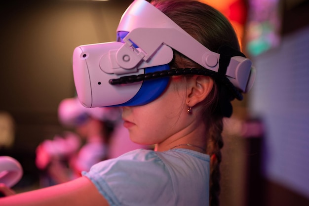 Vr-Spiel und Virtual-Reality-Kid-Girl-Gamer acht Jahre alt Spaß beim Spielen auf futuristischem Simulationsvideospiel in 3D-Brille und Joysticks in Unterhaltungs-VR-Raum-Innovationstechnologie und Neonlicht