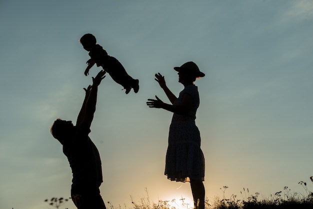 Vsilhouette der glücklichen Familie, die auf Klippe sich amüsiert