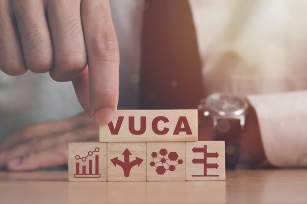 VUCA und strategisches Management Hand setzt Holzwürfel mit VUCA-Symbol und Text Volatilität Unsicherheit Komplexität Mehrdeutigkeit mit grauem Hintergrund Intelligentes Management für neue Trends und schnellen Übergang