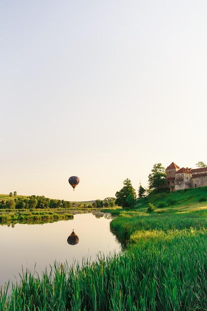 Vuelos en globo en la naturaleza. Hermoso globo aerostático volando sobre el lago cerca del castillo.