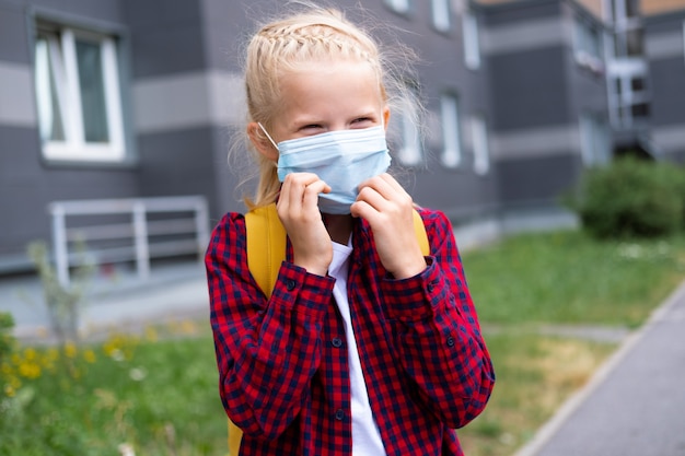 De vuelta a la escuela. Chica con máscara y mochilas protege y protege del coronavirus. Niño que va a la escuela después de la pandemia.