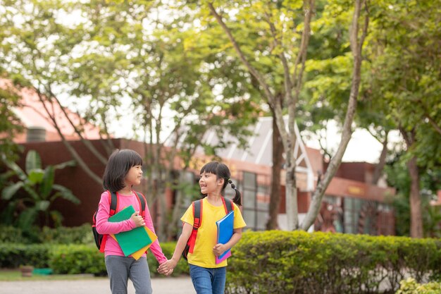 De vuelta a la escuela. Dos lindas niñas asiáticas con mochila escolar sosteniendo un libro y caminan juntos en la escuela