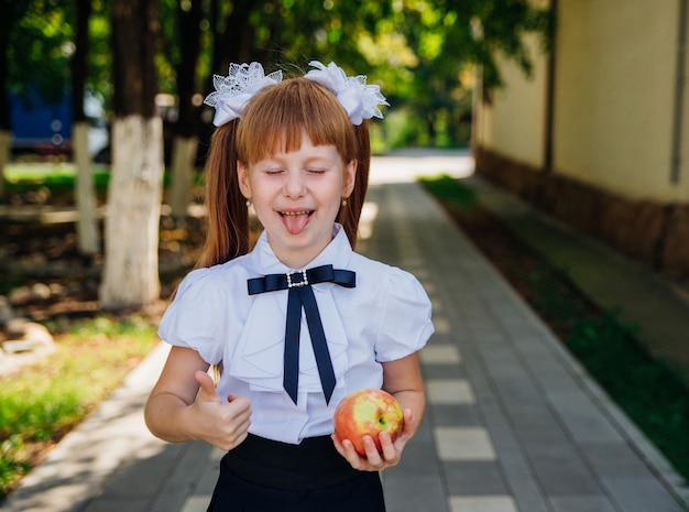 De vuelta a la escuela. Una linda colegiala está de pie en el parque o en el patio de la escuela y sostiene una manzana verde en sus manos. Comidas escolares adecuadas para el almuerzo.