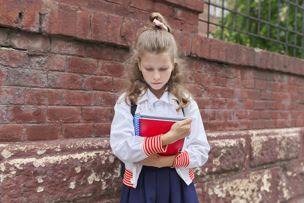 De vuelta a la escuela. Retrato al aire libre de la hermosa chica rubia cerca de la pared de ladrillo del edificio de la escuela valla