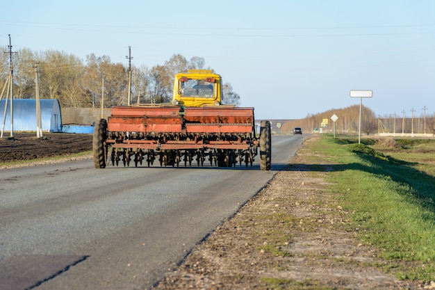Vuelve un tractor con cultivador con una campaña de siembra por un camino rural. El tractor bloqueó completamente la carretera. El transporte grande pasa por la carretera.