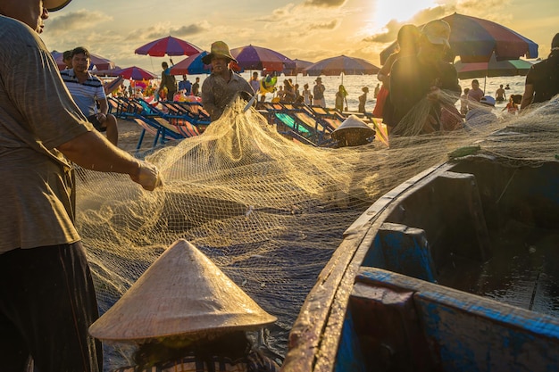 Vung Tau VIETNAM 20. AUG 2022 Fischer wirft sein Netz bei Sonnenaufgang oder Sonnenuntergang Traditionelle Fischer bereiten das Fischernetz vor Fischer am Strand beim Angeln