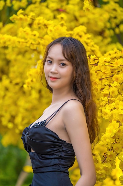 Vung Tau VIETNAM 7 DE ENERO DE 2023 Retrato de una hermosa mujer asiática vestida de negro parada cerca de Ochna Integerrima flor Tet vacaciones Año Nuevo Lunar