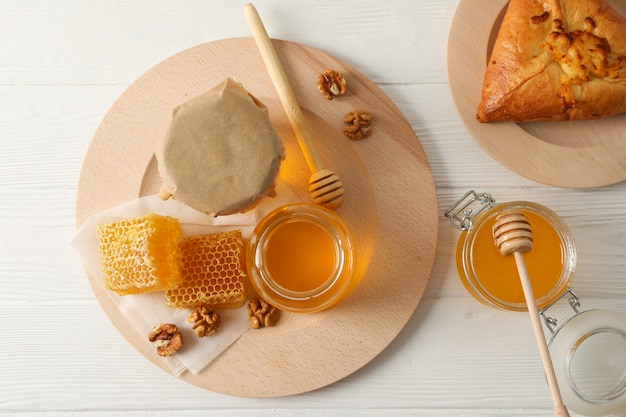 Waben, Walnüsse, Schöpflöffel, Gläser mit Honig und Brötchen auf hölzernem Hintergrund, Draufsicht