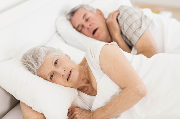 Wachen Sie ältere Frau im Bett auf, während ihr Ehemann schnarcht